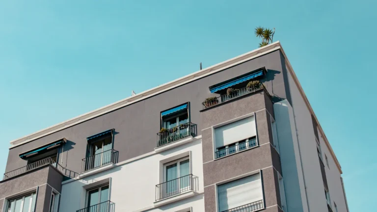 A modern multi-story apartment building with white and grey facades under a clear blue sky.