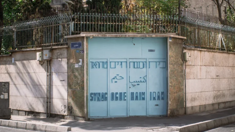 The entrance to a synagogue featuring a high security fence with metal spikes along the top of the perimeter wall.