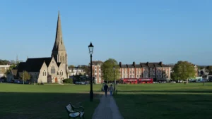 A scenic view of a park path, a historic church spire, and red buses in Redbridge.