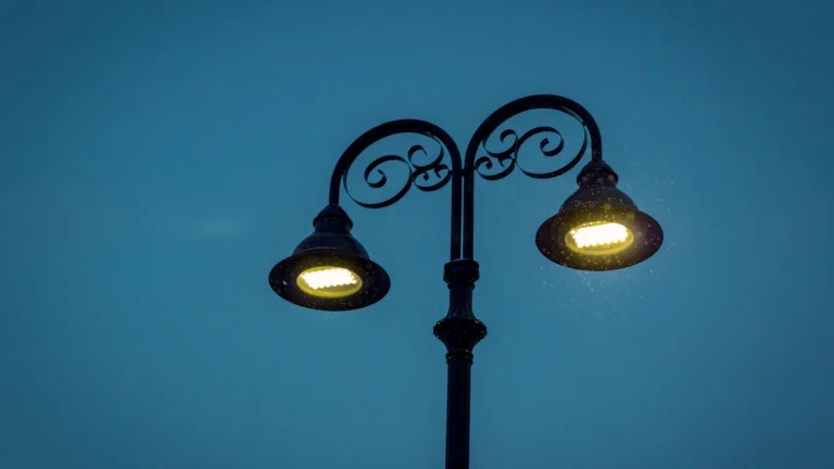 An ornate black double-headed street lamp glowing against a dark blue evening sky.