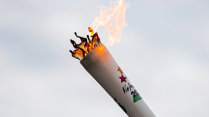 A white torch with vibrant orange flames burning brightly against a pale grey sky background.