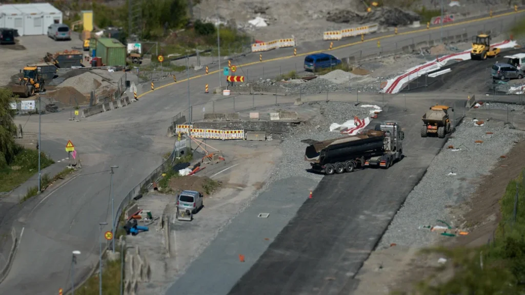 Aerial perspective of a large road construction site with heavy trucks and earthmoving machinery.