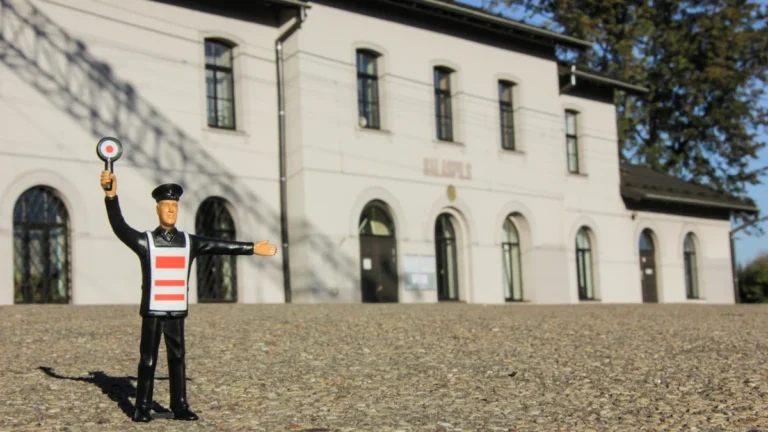 A small figurine stands before the white facade of the Salaspils railroad station in Latvia.