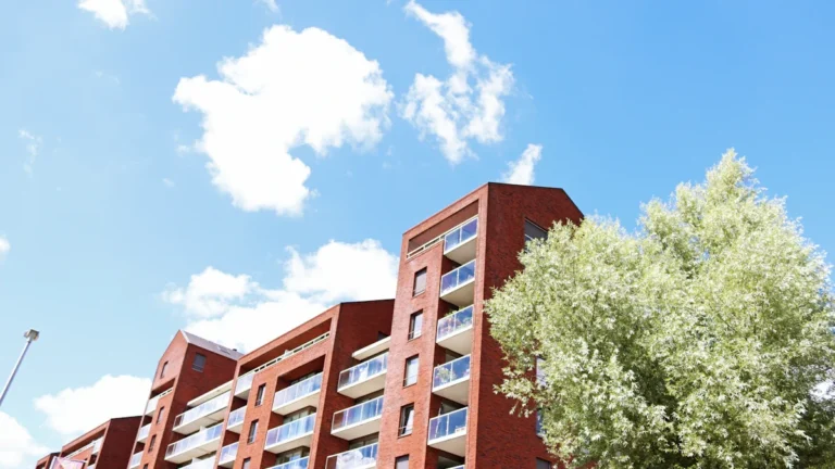 A modern red-brick apartment complex with white balconies under a bright blue sky.
