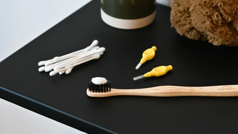 A wooden toothbrush, toothpaste tube, and a small brown teddy bear on a dark surface.