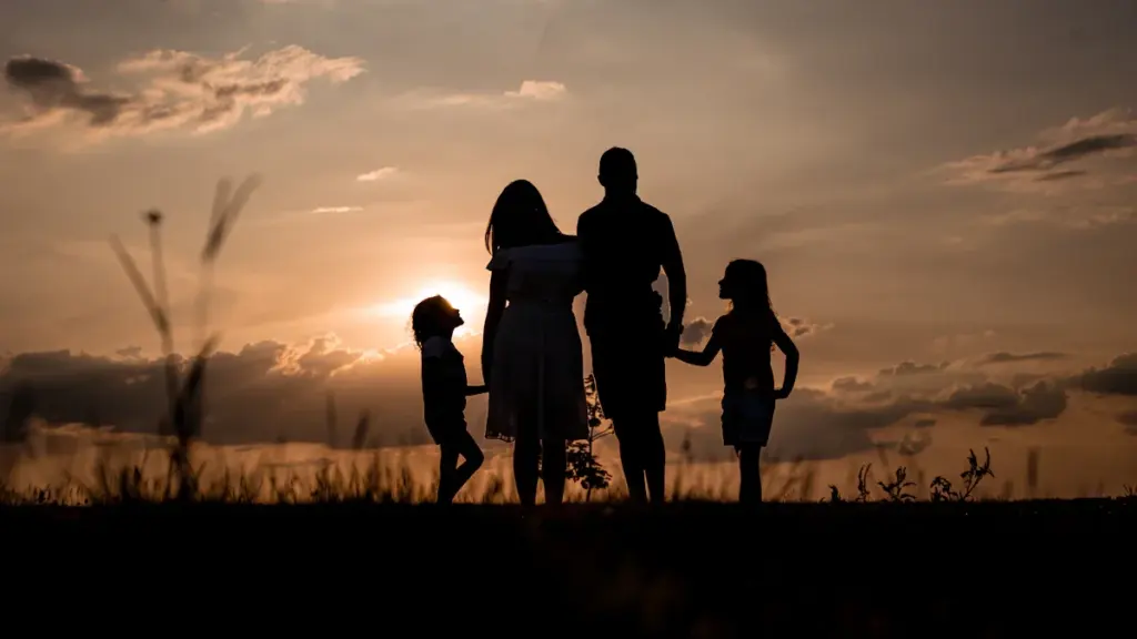 Silhouette of a family standing together in a grassy field during a sunset.
