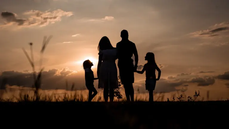 Silhouette of a family standing together in a grassy field during a sunset.