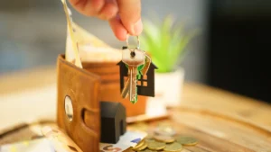 A hand holding house keys with a house-shaped keychain over a wallet and coins, symbolizing renter rights and financial protections.