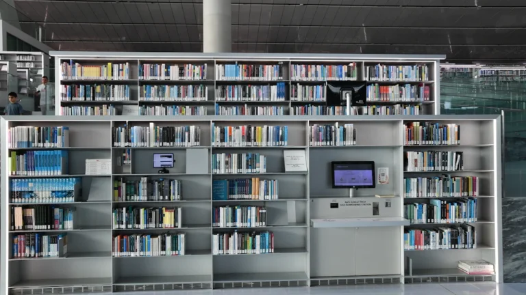 Rows of organized books on shelves in a bright, modern library with a digital computer terminal.
