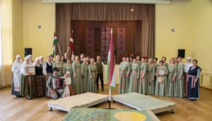 Large group in folk costumes posing with Hungarian and Latvian flags and an accordion player.