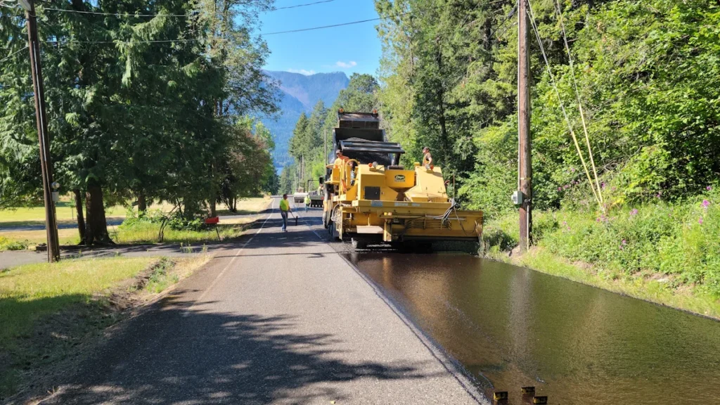 A road roller and maintenance truck resurfacing a rural road with fresh tarmac.
