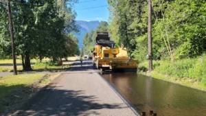 A road roller and maintenance truck resurfacing a rural road with fresh tarmac.