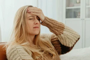 Blonde woman in a sweater holding her hand to her forehead with her eyes closed tightly.