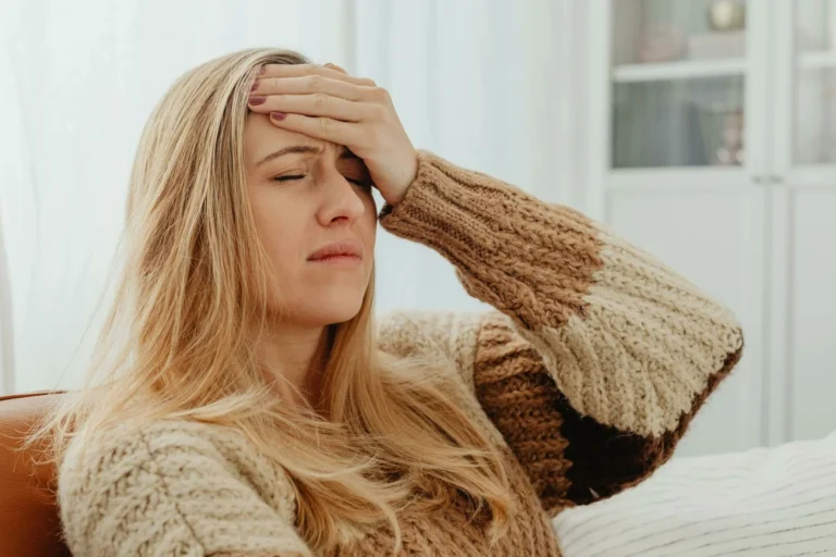 Blonde woman in a sweater holding her hand to her forehead with her eyes closed tightly.