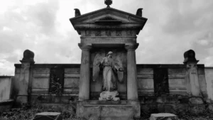 A black and white photo of a weathered stone tomb featuring a central angel statue.