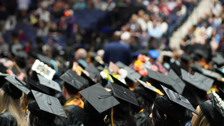 A large crowd of graduates wearing black caps and gowns during a ceremony, representing the Smiltene Municipality graduation events.
