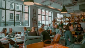 A bustling indoor scene of a modern UK café with customers chatting and working at wooden tables.