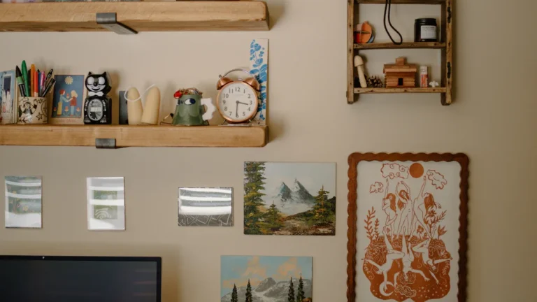 A cream-colored wall featuring wooden floating shelves decorated with eclectic art, small sculptures, and stationery.