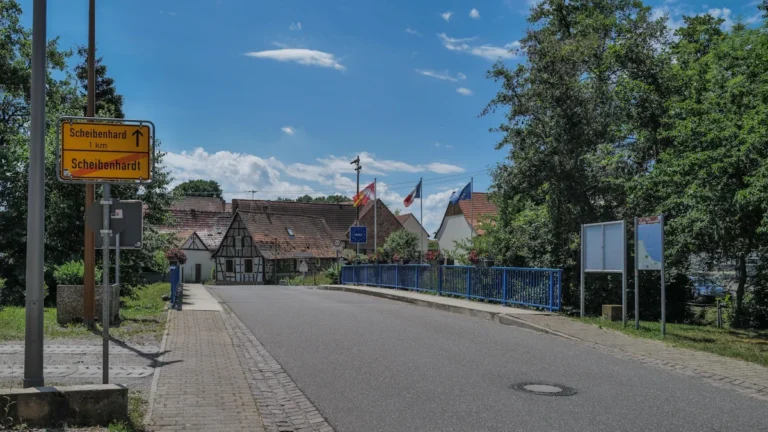 A bridge at the Franco-German border showing signs for the towns of Scheibenhardt and Scheibenhard with French, German, and European Union flags flying in the background.