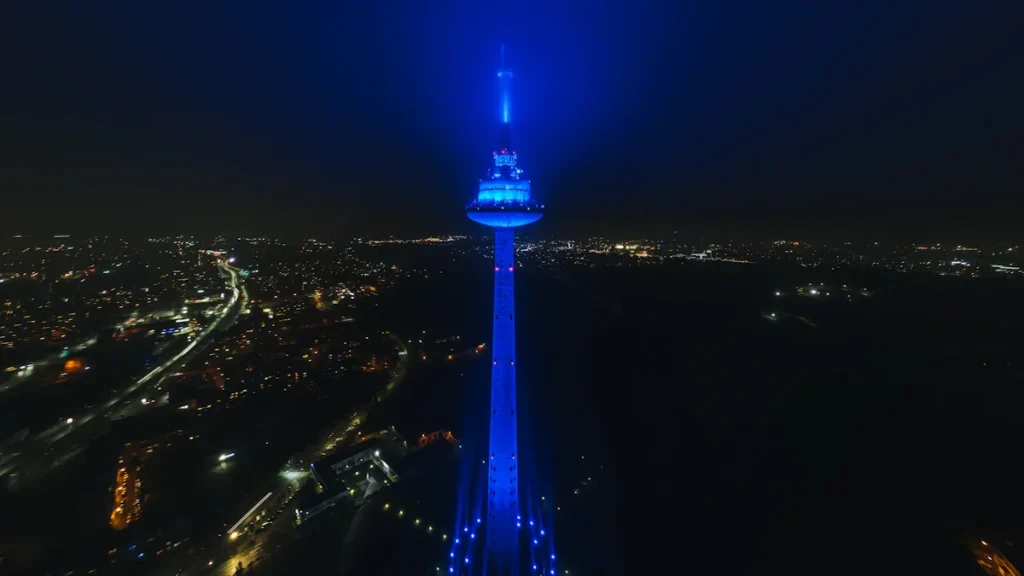 A tall communication tower illuminated in bright blue light against a dark night sky in Vilnius.