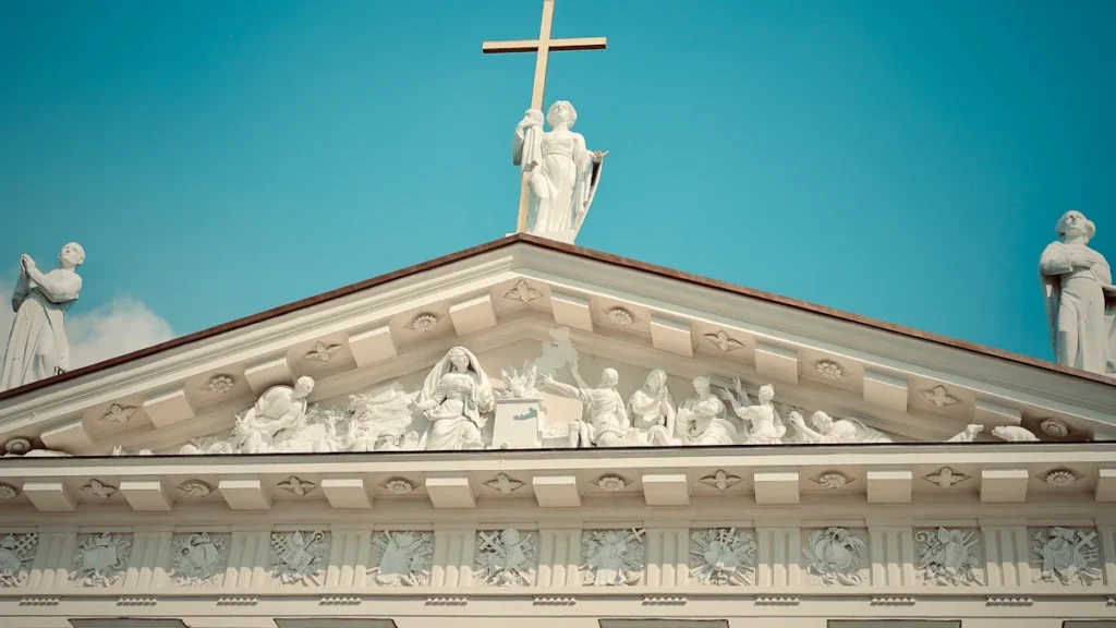 The neoclassical pediment and religious statues atop the white facade of Vilnius Cathedral in Lithuania.