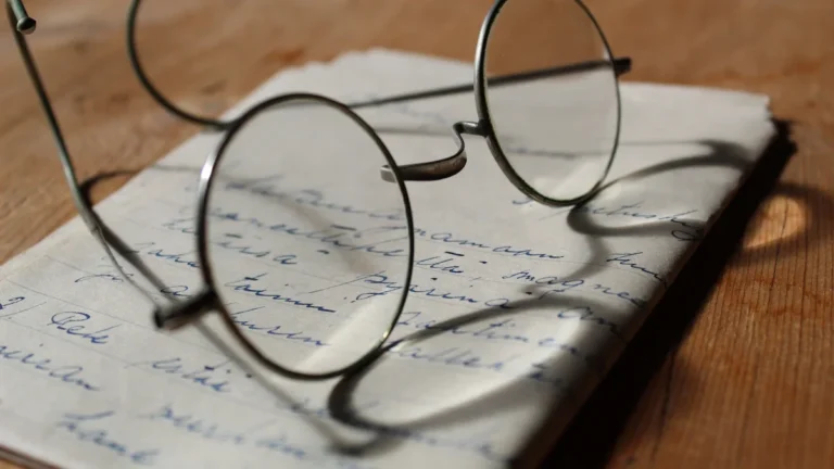 Vintage wire-rimmed spectacles resting on an old handwritten letter with cursive script on a wooden desk.