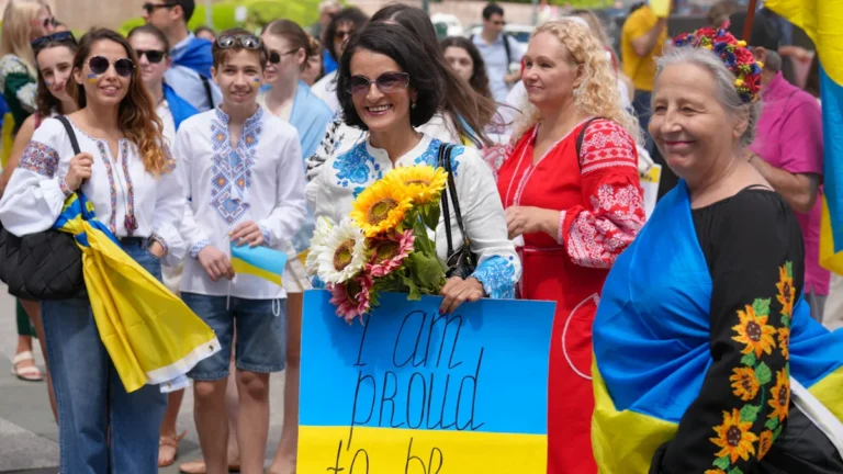 A celebratory crowd in Kaunas for Ukrainian Vyšyvanka Day, featuring a woman holding a yellow and blue sign that says 'I am proud to be Ukrainian!'