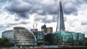 The London skyline featuring the former City Hall and The Shard against a cloudy sky.