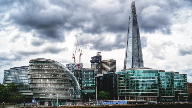 The London skyline featuring the former City Hall and The Shard against a cloudy sky.