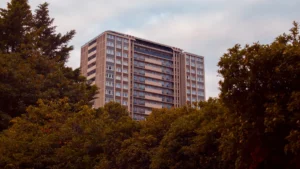A large white residential apartment building in London partially framed by green trees during the day.
