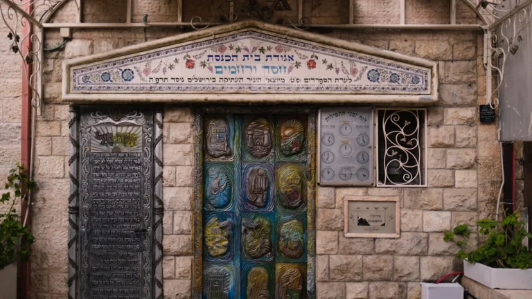The stone entrance and decorative doors of a synagogue featuring Hebrew inscriptions.