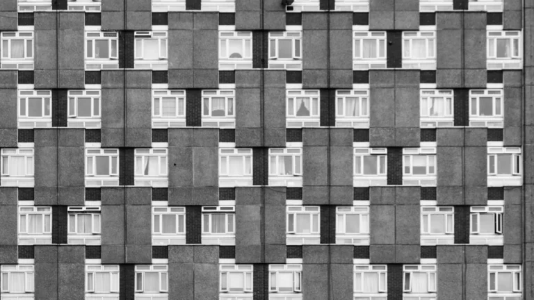 A black and white architectural photograph showing the repetitive facade and windows of a social housing block in Tower Hamlets.