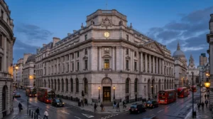 Historic stone building on a London street corner with red buses and taxis at dusk.