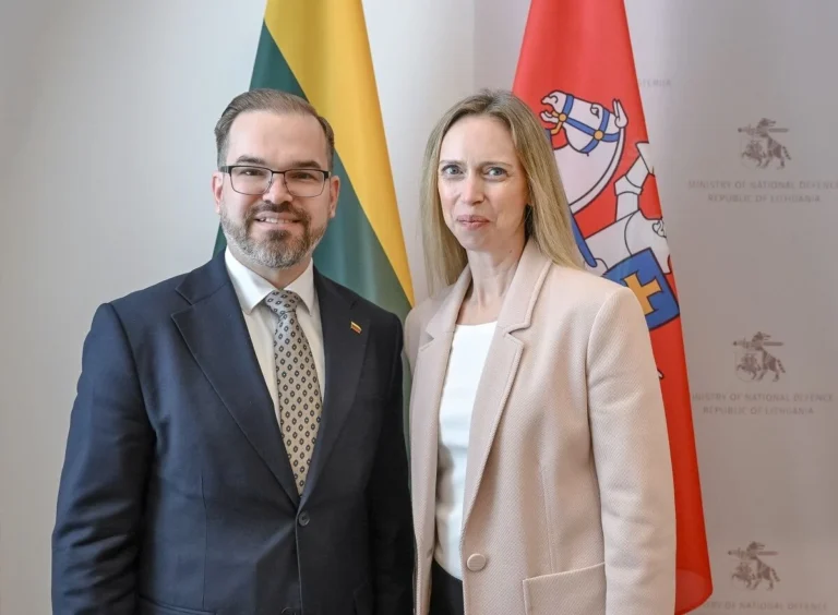 A man and woman standing together in front of two Lithuanian official flags.