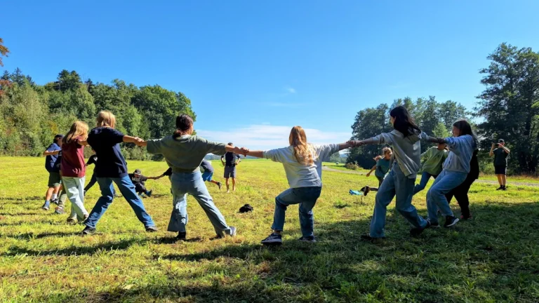 Children playing tug of war in a sunny green field at a summer camp.
