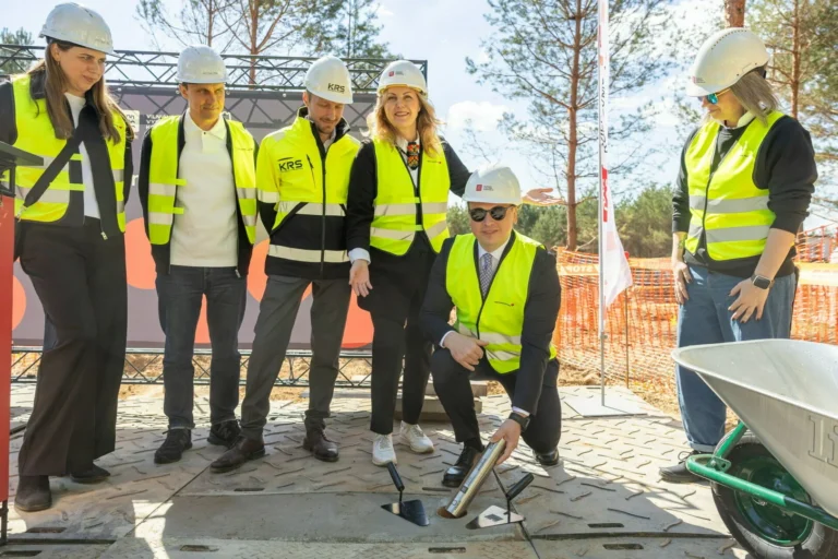 Six people in hard hats and safety vests during a ceremonial time capsule burial ceremony.