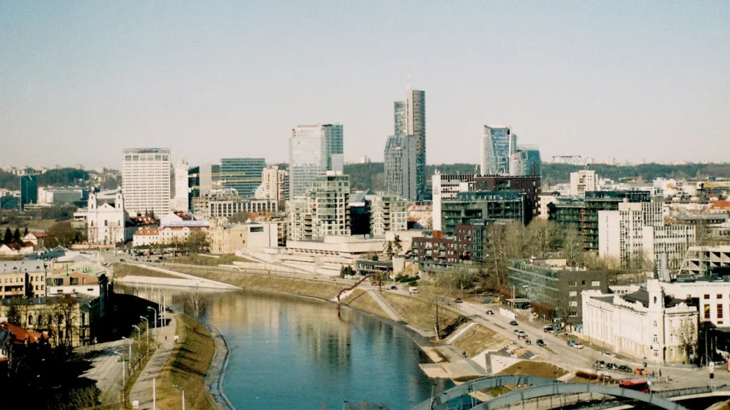 A wide-angle view of the modern Vilnius skyline and Neris River under a clear blue sky.