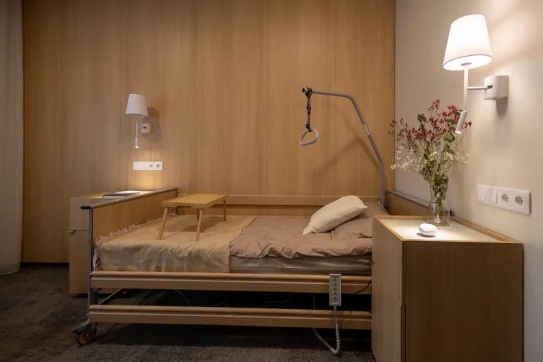 Modern adjustable hospital bed with overhead trapeze bar and wooden tray in a warm room.