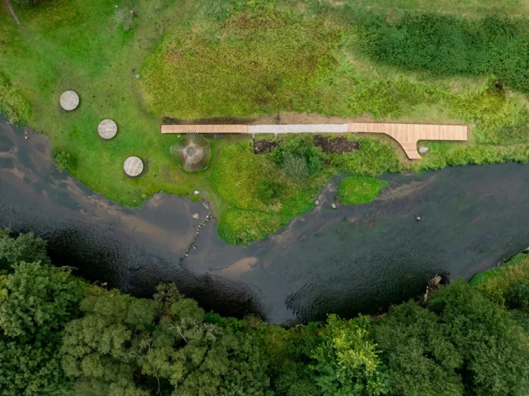 Aerial view of a wooden walkway and circular platforms along a lush green riverbank.