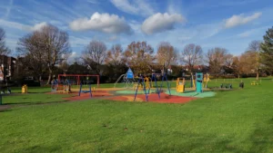 A colorful and well-maintained public children's playground with climbing frames and swings under a clear blue sky.