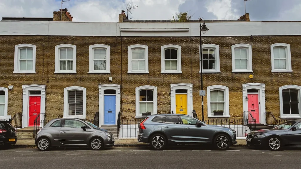A row of London terraced houses with white window frames and colorful doors under a cloudy sky.