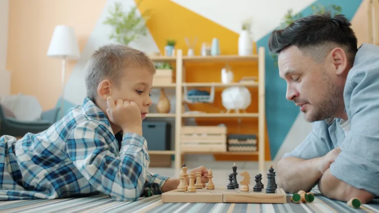 A foster father and son share a focused moment playing chess together on the floor of their home.