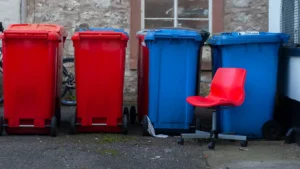 A row of red and blue residential wheelie bins lined up against a stone wall.