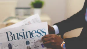 A person in a professional suit holding a newspaper with a large 'Business' headline.