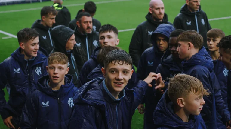 A group of young football players in training jackets standing together on a field, representing community and team support.