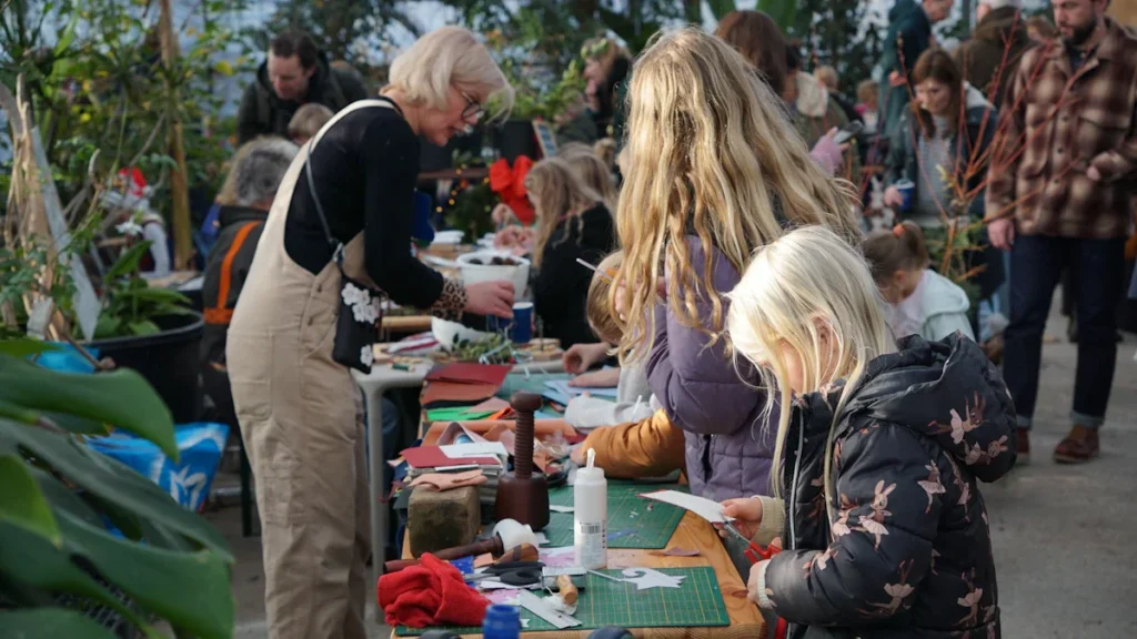 A multi-generational group of residents participating in a creative community workshop in a garden setting.