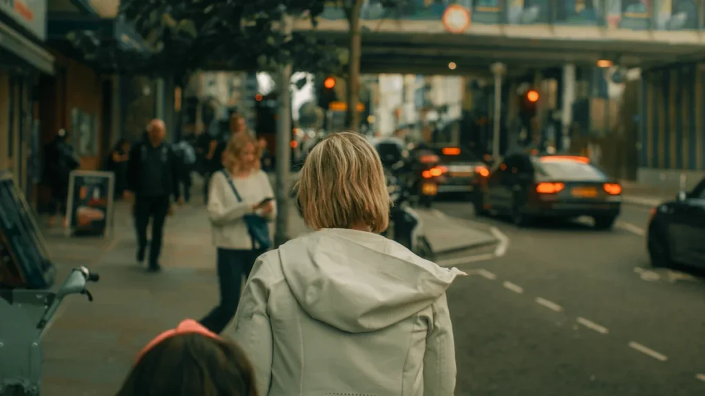 A woman and a child walking along a busy UK high street with traffic in the background.