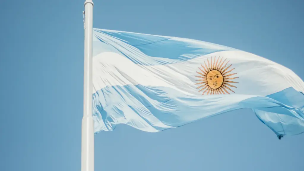 The blue and white striped national flag of Argentina waving against a clear sky.