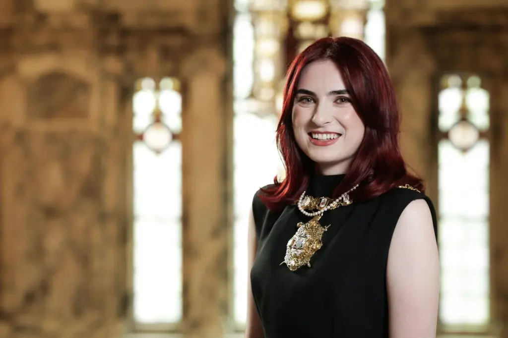 A smiling woman with red hair wearing a black dress and formal ceremonial chain.