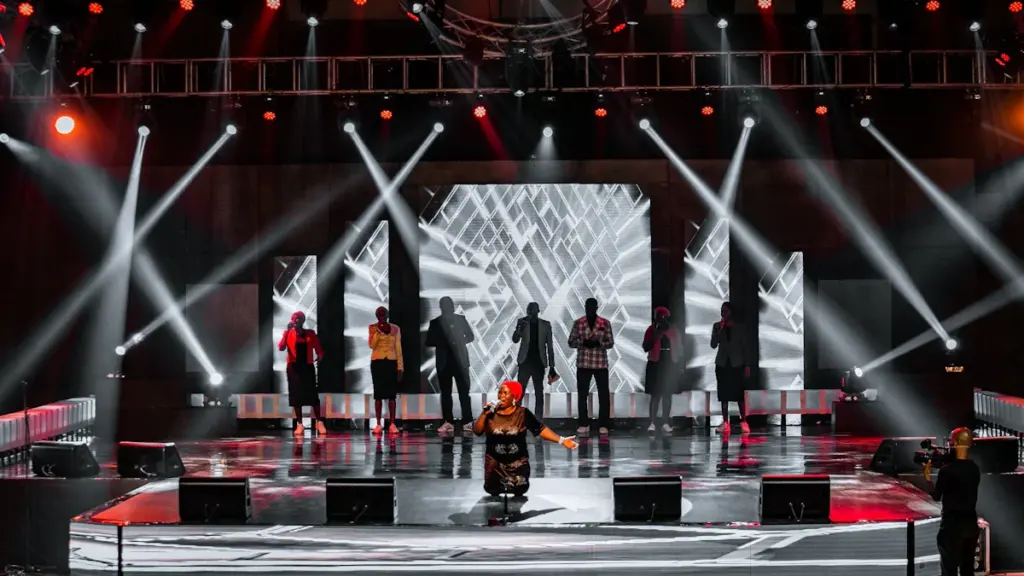 People performing on a brightly lit stage under dramatic theatrical spotlights.